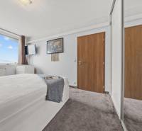 Světlá ložnice s postelí, velkým oknem a šatní skříní v 2pokojovém bytě.