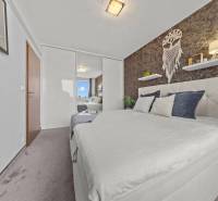 Ložnice v 2pokojovém bytě s manželskou postelí, zrcadlovou skříní a dekoracemi na stěně.