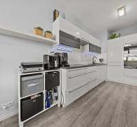 Kuchyně v 2-pokojovém bytě s bílými skříňkami a podlahou s dřevěným dekorem.