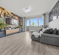 Obývací pokoj s pohodlným gaučem, tapetou s rostlinným motivem a podlahou s dřevěným dekorem.