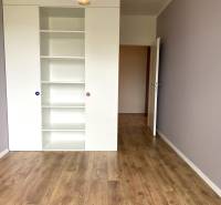 Pokoj s bílým regálem a podlahou s dřevěným dekorem ve 3-pokojovém bytě.