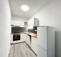 Kuchyně v 1-pokojovém bytě s černým obkladem a podlahou s dřevěným dekorem.