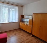 Pokoj v 3-pokojovém bytě se starším nábytkem a podlahou s dřevěným dekorem.