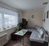 Obývací pokoj v rodinném domě s gaučem, stolem a oknem se záclonou.