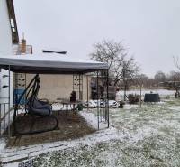 Zasněžená zahrada u rodinného domu na Nové ulici ve Velkých Ozorovcích s altánkem.