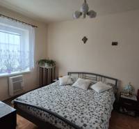 Ložnice v rodinném domě se vzorovaným přehozem, televizí a podlahou s dřevěným dekorem.