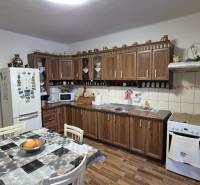 Kuchyně v rodinném domě s kuchyňskou linkou, jídelním stolem a podlahou s dřevěným dekorem.