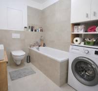 Koupelna v 1-pokojovém bytě s vanou, pračkou a toaletou, doplněná úložným prostorem.