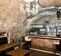 Starobylý styl v gastro prostorech s cihlovým barem a knihami pod lustrem.