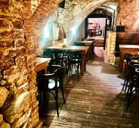 Kamenné oblouky, dřevěné stoly a podlaha s dřevěným dekorem v gastro prostorech.