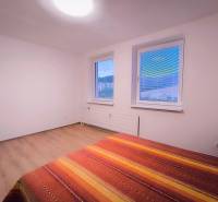 Světlý pokoj se dvěma okny, postelí a podlahou s dřevěným dekorem.