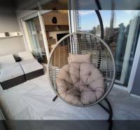 Odpočinková terasa rekreačního apartmánu s kulatým houpacím křeslem a ratanovým posezením.