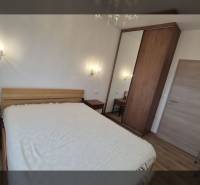 Rekreační apartmán s pohodlnou postelí a podlahou s dřevěným dekorem, osvětlený nástěnnými lampami.