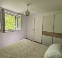 Světlá ložnice s oknem, bílou stěnou a skříní v rodinném domě.