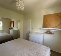 Ložnice v rodinném domě s bílým nábytkem, zrcadlem a texturovanými přehozy na postel.