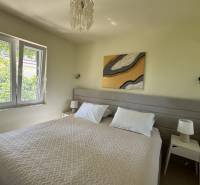 Ložnice v rodinném domě s manželskou postelí, stolky s lampami, velké okno.