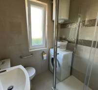 Koupelna v rodinném domě se sprchovým koutem, pračkou a oknem.