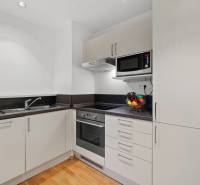 Kuchyně v 2-pokojovém bytě s bílými skříňkami a podlahou s dřevěným dekorem.