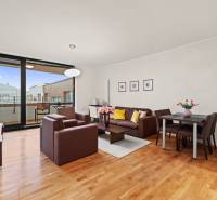 Obývací pokoj dvoupokojového bytu s posezením, jídelním stolem a podlahou s dřevěným dekorem.