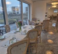 Útulné gastro prostory s elegantním prostíráním, květinami a velkými okny.