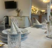 Prostřené stoly v gastro prostoru s televizorem, zlatými dekoracemi a elegantním stolováním.