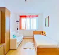 Pokoj v 3-pokojovém bytě s podlahou s dřevěným dekorem, nábytkem a velkým oknem.