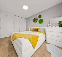 Světlá ložnice s postelí, bílým nábytkem, rostlinami a podlahou s dřevěným dekorem ve 4-pokojovém bytě.