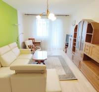 Obývací pokoj v 2-pokojovém bytě s krémovou sedačkou, zelenou stěnou a sestavou.