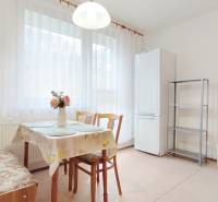 Kuchyně v 2-pokojovém bytě s jídelním stolem, židlemi a lednicí.