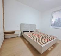 Ložnice v 2-pokojovém bytě s podlahou s dřevěným dekorem, velké okno, postel a úložný prostor.