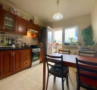 Kuchyně v 3-pokojovém bytě s dřevěnými skříňkami, jídelním stolem a oknem na balkon.