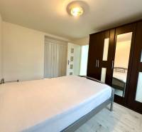 Ložnice v 2-pokojovém bytě s postelí, skříní a podlahou s dřevěným dekorem.