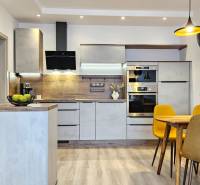 Kuchyně v 1-pokojovém bytě s podlahou s dřevěným dekorem, jídelní stůl a žluté židle.