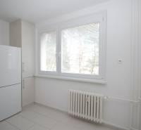 Pokoj v 3-pokojovém bytě s bílými stěnami, radiátorem a lednicí.