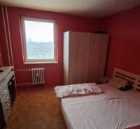 Ložnice v 3-pokojovém bytě s postelí, skříní a komodou na červené stěně.