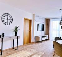 Obývací pokoj ve 3pokojovém bytě s podlahou s dřevěným dekorem, stolem a televizí.