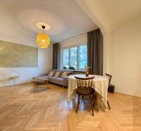 Obývací pokoj v 2pokojovém bytě s hnědou sedačkou a podlahou s dřevěným dekorem.