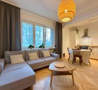 Obývací pokoj s kuchyní a jídelním stolem, podlaha s dřevěným dekorem, světlá sedačka.