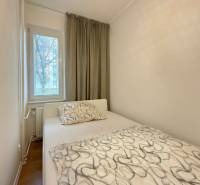 Ložnice v 2-pokojovém bytě s postelí, oknem a závěsy, podlaha s dřevěným dekorem.