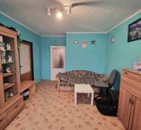 Pokoj v 3-pokojovém bytě s tyrkysovými stěnami, hnědým nábytkem a vzorovaným kobercem.