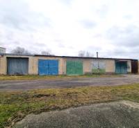 Budova se sérií pestrých garážových vrat v Kuklově, vedle asfaltové cesty.