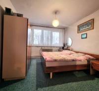 Ložnice v 3-pokojovém bytě s dvojlůžkem, koberec, nábytek a záclony na okně.