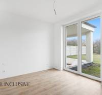 Pokoj v rodinném domě s velkým oknem a podlahou s dřevěným dekorem.