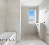 Koupelna v rodinném domě s vanou, oknem a světlými obklady.