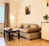 Obývací pokoj v 2pokojovém bytě s béžovou sedačkou, podlaha s dřevěným dekorem.