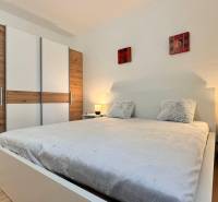 Ložnice v 2-pokojovém bytě s velkou postelí, šatní skříní a podlahou s dřevěným dekorem.