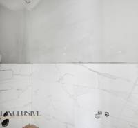 Koupelna v rodinném domě s bílými mramorovými obklady bez zařizovacích předmětů.