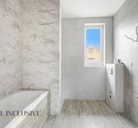 Koupelna v rodinném domě s vanou, šedými obklady a podlahou s dřevěným dekorem.