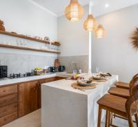 Kuchyně vily se stylovými dřevěnými prvky, barovými stoličkami a závěsnými lampami.
