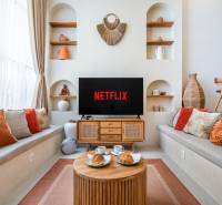 Pohodlný obývací pokoj ve vile s televizí, polštáři a dekoracemi, podává se káva.